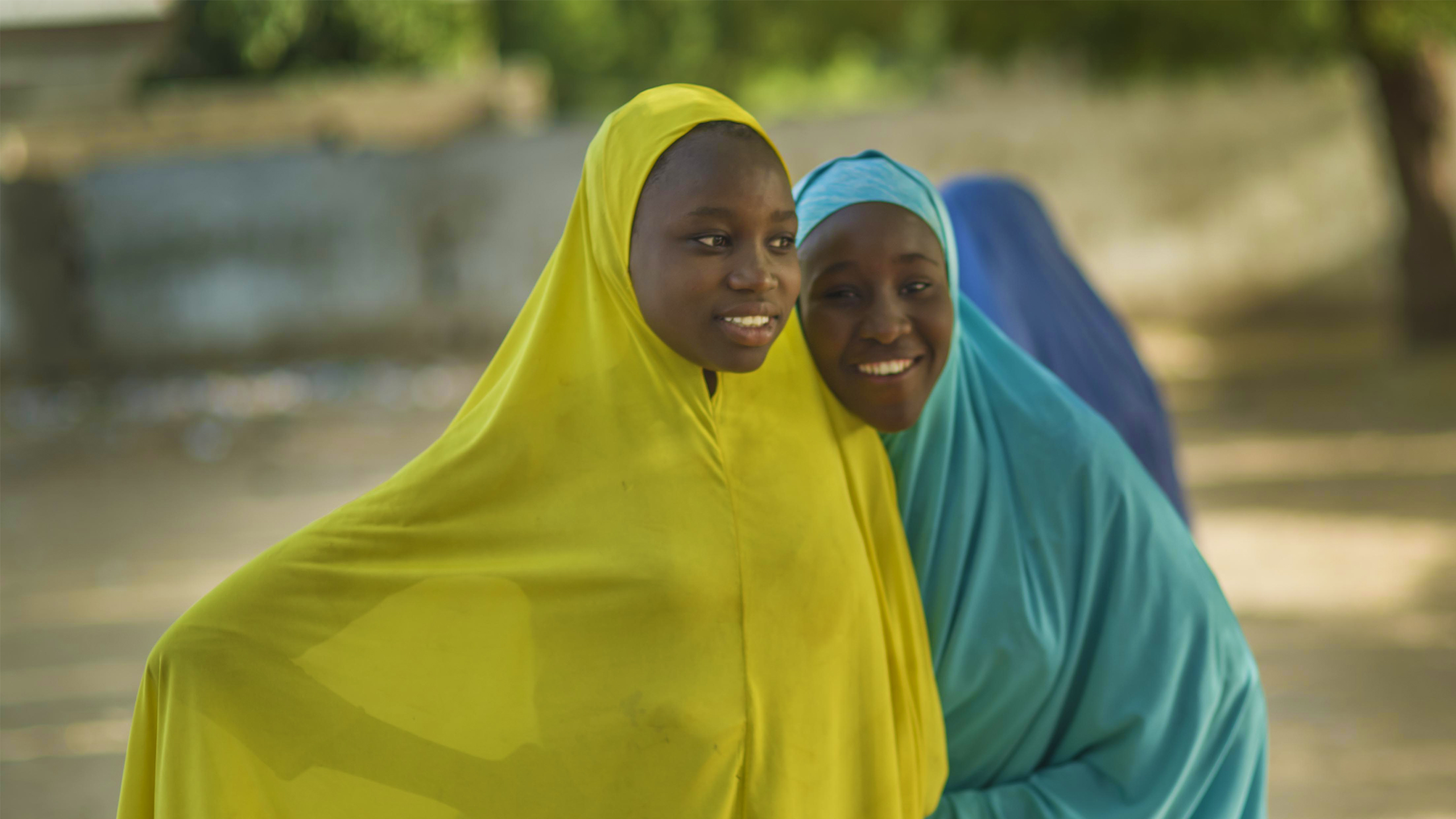 MAG - Freeing people from fear. Two young girls wearing brightly coloured covering smiling for the camera.