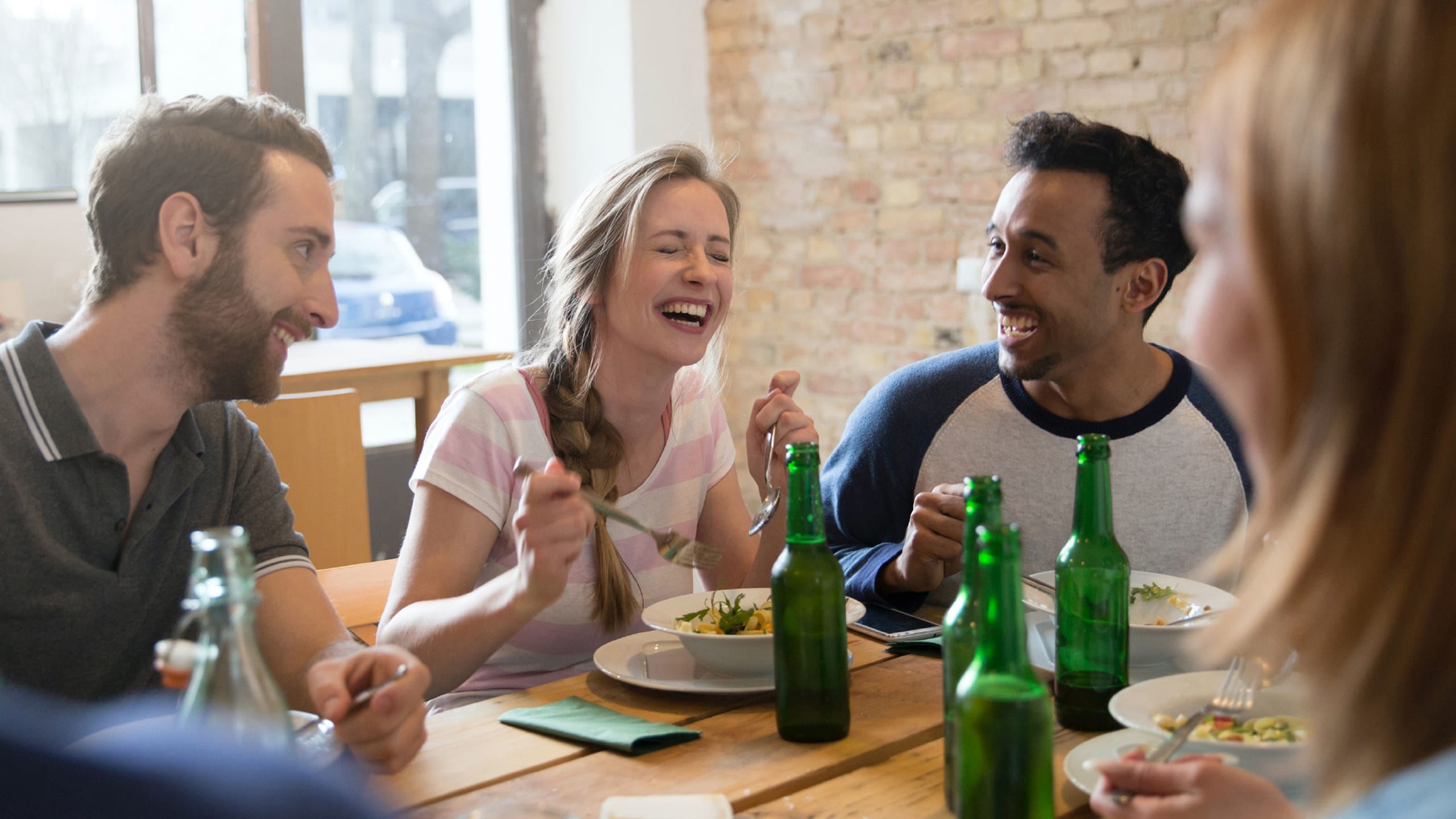 Leeds Building Society - Creating a welcoming society. Group of friends sat in a restaurant enjoing a meal together while laughing.